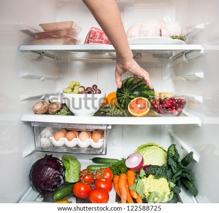 Human Arm Reaching for Orange Fruit in Open Refrigerator Full of Healthy Food
