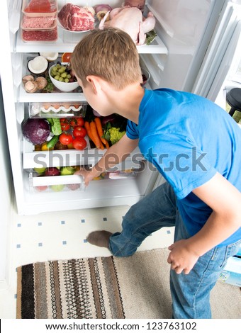 Young Boy Reaching for Snack in Refrigerator Full of Healthy Food Options