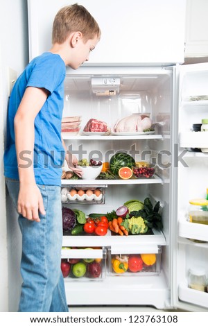 Young Boy Reaching for Snack in Refrigerator Full of Healthy Food Options