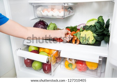 Hand Reaching for Carrot in Refrigerator Full of Healthy Food Options