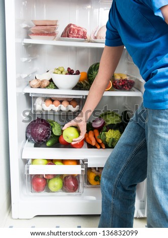 Hand Reaching for Green Apple in Refrigerator Full of Healthy Food Options