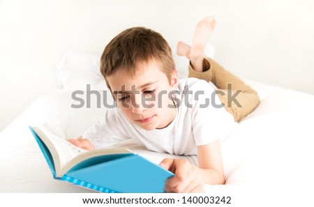 Young Boy Reading Blue Book in Bed