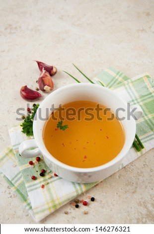 Bone Broth in Small Soup Bowl Served with Fresh Herbs, Garlic and Spices