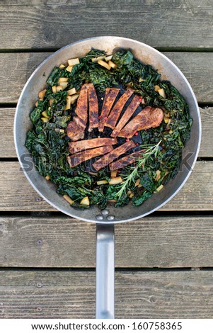 Grass Fed Beef Steak Seared and Sliced Served with Wilted Kale on Stainless Steel Skillet