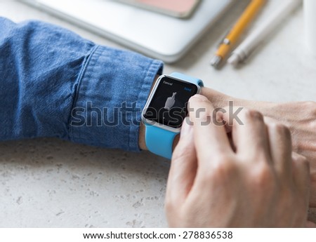 SEATTLE, USA - May 17, 2015: Man Wearing Sport Apple Watch with Blue Rubber Band. Fingers Crossed Emoji Displayed.