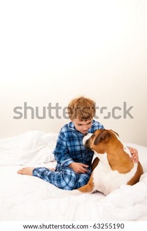 Young Boy in Blue Pajamas Talking to His Dog on Bed with White Sheets