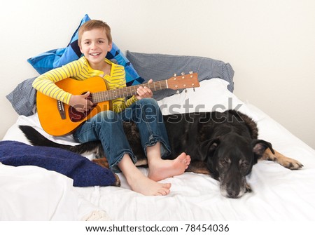 Young Child in Bed Playing Guitar to His Old Dog
