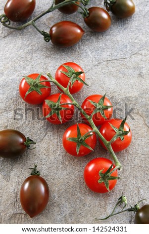 Red and tiger cherry tomatoes, on a gray slate stone.