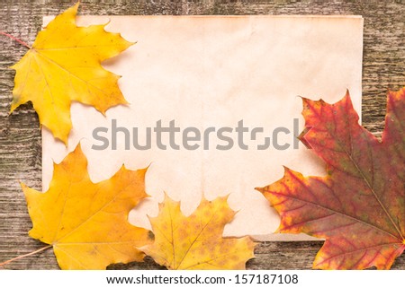 Old paper sheet with fallen leaves on wood background