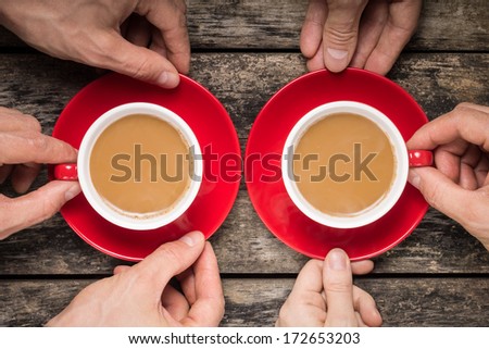 Hands Taking Two Red Cups of Coffee on old Wood Background