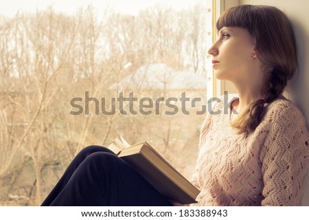 Young adult girl reading book near the window. Warm toned image