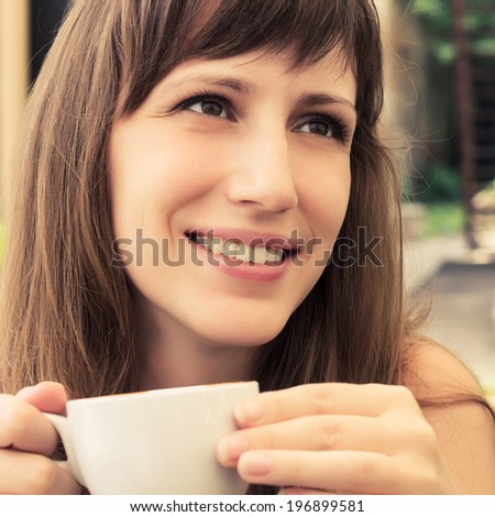 Portrait of young woman dreaming in cafe. Chatting attractive girl with cup of coffee. Warm color toned image