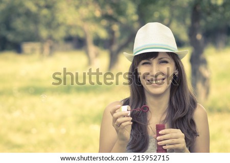 Young woman making soap bubbles in summer park. Caucasian hipster girl in hat blowing soap bubbles at midday