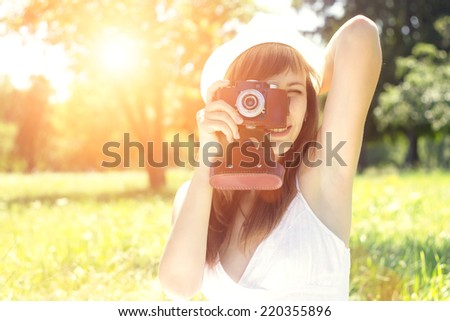 Beautiful hipster woman posing with old film camera in summer park with sunbeams.