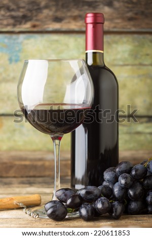 Winery background. Dark blue grapes with bottle of red wine and glass on wooden background