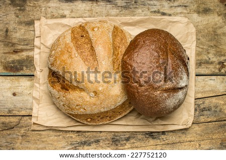 Loafs of different species of bread on wood background with paper bag. Top view