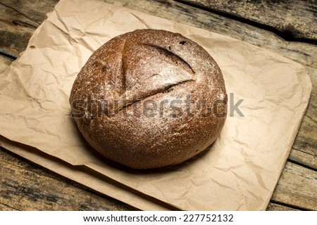 Fresh baked loaf of bread on paper bag at old wooden table