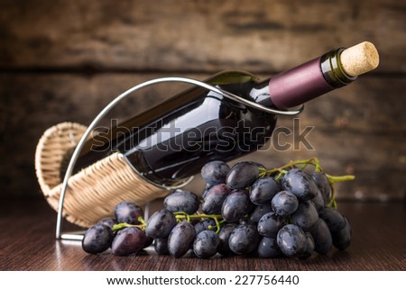 Red wine with cluster of dark blue grapes at wooden table. Winery still-life on wood background