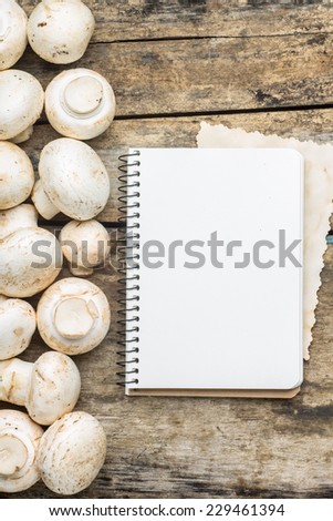 Mushrooms with blank cooking book or recipe sheet on wood background