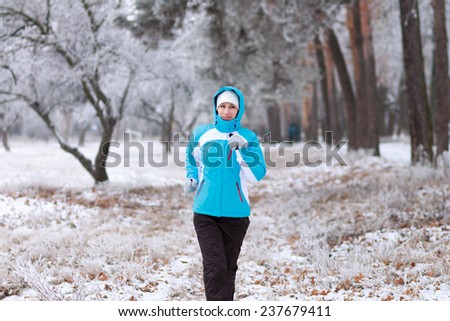 Smiling young woman jogging at winter park. Outdoor sport healthy running