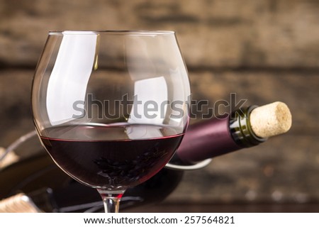 Red wine in wineglass against corked bottle on wood background