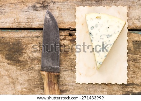 Blue cheese background with copyspace. Piece of cheese with old knife on wooden table