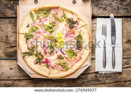 Tasty Pizza in open box served with silverware on old wooden table. Top view image fast food background