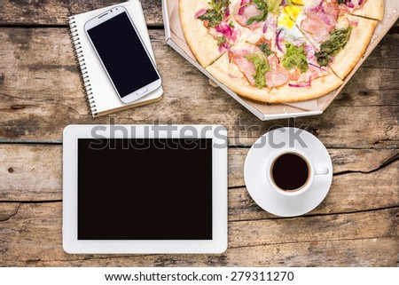 Remote freelance workplace coffee break. Outsource workspace with tablet PC, smartphone and pizza with coffee. Top view image