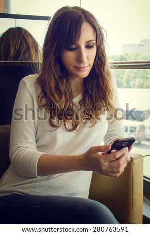 Young cheerful woman sitting in restaurant using smartphone. Warm color toned image of pretty girl with gadget in cafe