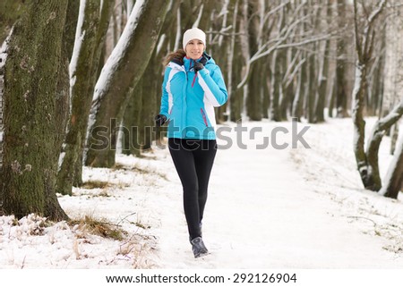 Young sport woman jogging in winter park. Sportswoman running on snowy pathway