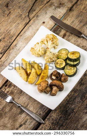 Roasted vegetables with sauce served on wooden table. Restaurant menu background