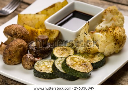Roasted vegetables with sauce served on wooden table. Recipe or menu background