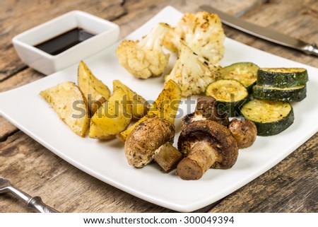 Roasted vegetables with sauce served on wooden table. Vegetarian menu background