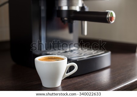 White ceramic cup of espresso with coffee ma?hine on the table. Brewing coffee at work