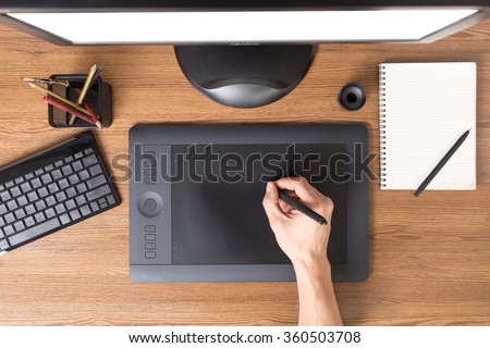 Designer using graphic tablet in the office. Top view workplace with tablet, keyboard and computer.