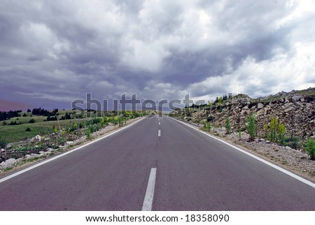 gray road through mountain landscape under cloudy sky