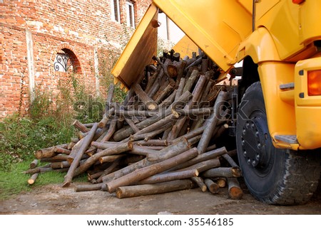 unloading wood delivery from yellow truck by brick house