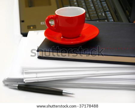 red coffee cup over black notebook on office desk