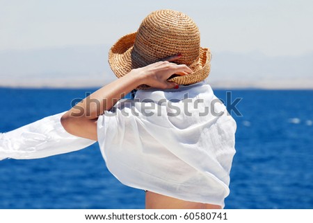 woman head and arms in straw hat from back over blue sea