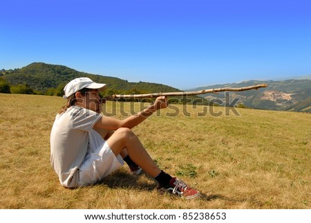 boy sitting on mountain meadow aiming with a stick as a gun