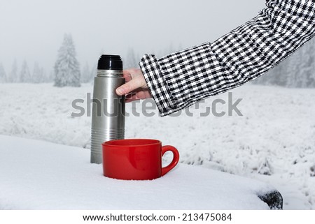 Hand filling in winter landscape cup with hot drink