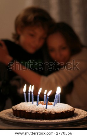 Birthday wishes - Serene siblings sharing a precious moment in front of the lighted candles.  The focus is on the front of the cake.