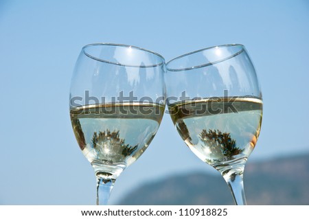 Two wineglasses filled with white wine clinking each other outside on a summer day.