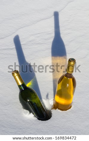 Two colorful bottles of wine chilling in the snow with long shadows