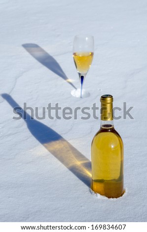 White wine in glass & bottle with long shadows on the snow