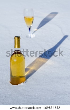 White wine in glass & bottle with long shadows on the snow