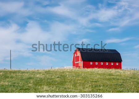 Traditional red barn with white trim in open pasture with blue sky & a few clouds