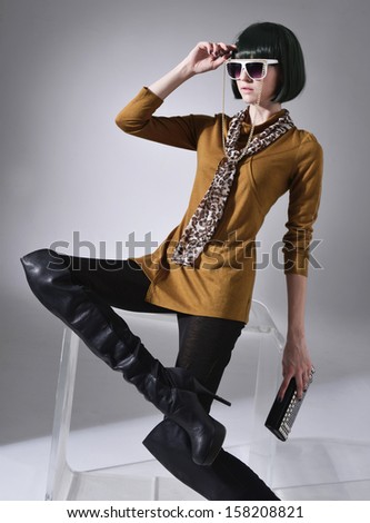 fashionable girl in sunglasses with purse ,scarf sitting cube in studio