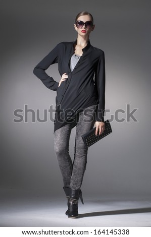 Full length fashion girl wearing modern sunglasses holding purse walking in studio