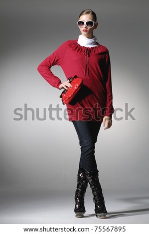 Beautiful high fashion model in modern clothes hold purse posing on lightbackground